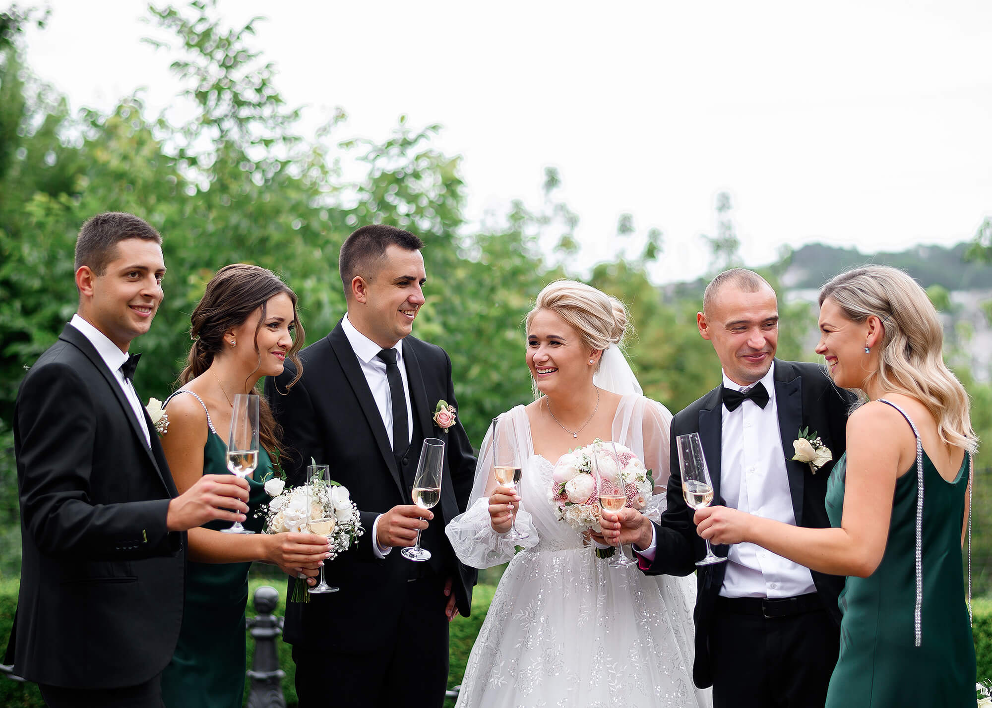 cheerful newlyweds and their friends holding glasses with champagne celebrating the wedding day